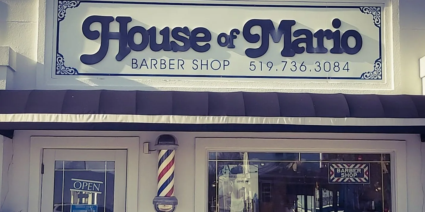 The House of Mario Barber Shop storefront: cream sign, navy awning and a red, white and blue barber pole by the door